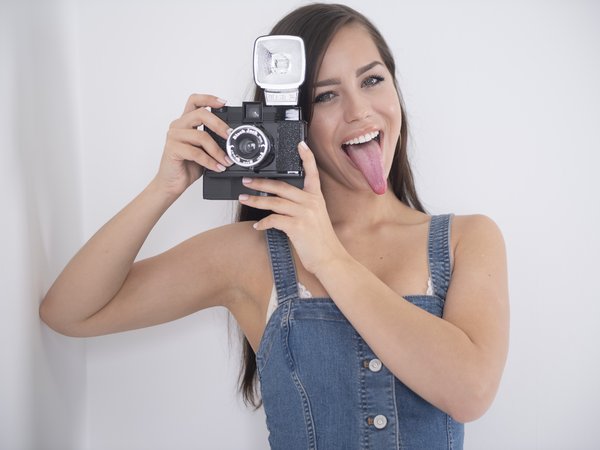 Alina Lopez, armpits, bare shoulders, brown hair, brunette, camera, denim dress, dress, face, girl, green eyes, lips, long hair, looking at camera, looking at viewer, model, mouth, open mouth, photo, pornstar, portrait, simple background, straight hair, strap, tongue