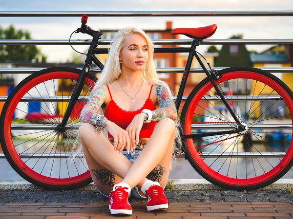 bicycle, blonde, blue eyes, fence, girl, jean shorts, legs, legs crossed, lips, looking away, model, mouth, necklace, photo, portrait, red top, short shorts, shorts, sneakers, socks, tank top, tattoo