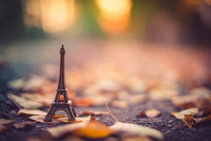 Обои на рабочий стол: La tour Eiffel, асфальт, боке, листья, осень, подставка, размытость, статуэтка, сухие, эйфелева башня